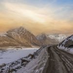 A panoramic view of a winding road through snowy mountain landscape at sunrise/sunset on the Leh to Hunder route.