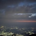 A night view from Triund top showcasing the illuminated Dharamshala Valley and Kangra Valley, with a contrast of dark hills and a twilight sky.
