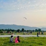 A serene view of Billing landing site with visitors enjoying the open space as one paraglider soars above during sunset. during Bir Billing Package