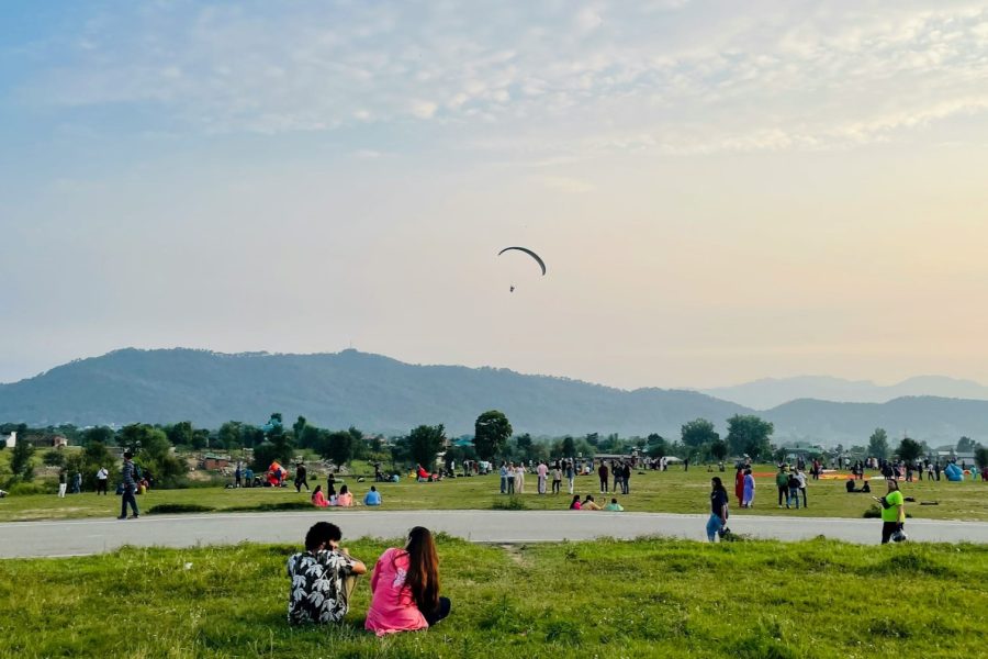 A serene view of Billing landing site with visitors enjoying the open space as one paraglider soars above during sunset. during Bir Billing Package