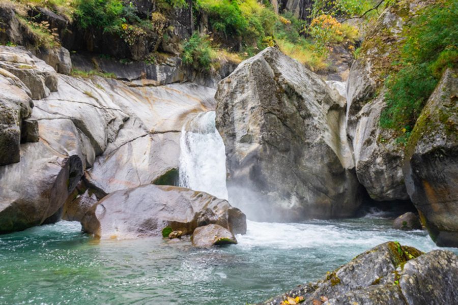 A tranquil waterfall flows through smooth boulders surrounded by greenery at Hippo Falls in Great Himalayan National Park’s Jibhi Tirthan Valley.