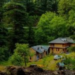 A beautiful mud house in Jibhi Tirthan, surrounded by lush greenery, with a thatched roof and wooden beams. Jibhi Tour Package