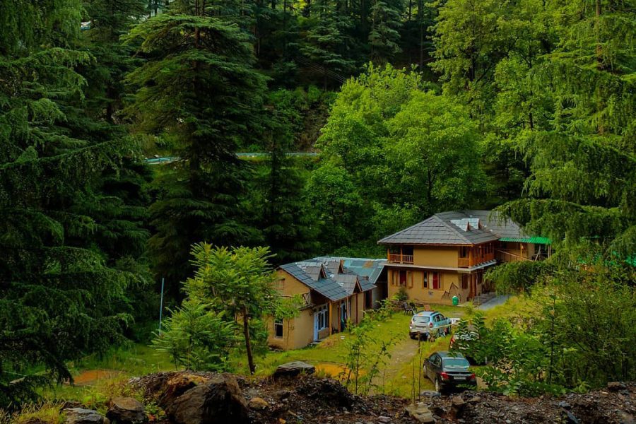 A beautiful mud house in Jibhi Tirthan, surrounded by lush greenery, with a thatched roof and wooden beams. Jibhi Tour Package