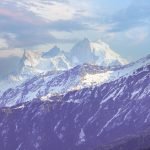 Snow-covered peaks of the Yamunotri range viewed from the Kedarkantha peak summit under a partly cloudy sky.