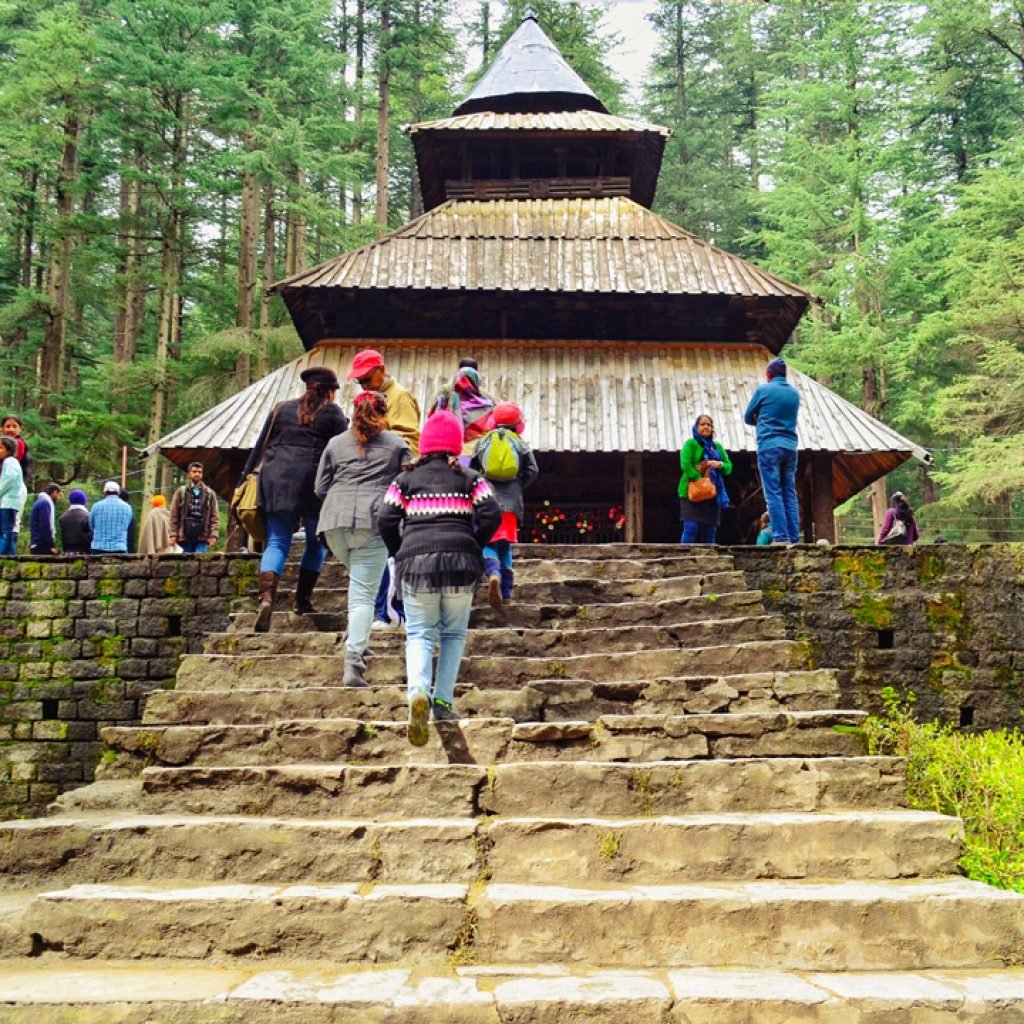 Visitors at the Hadimba Devi Temple during the Manali Kasol Package, surrounded by a lush green forest.