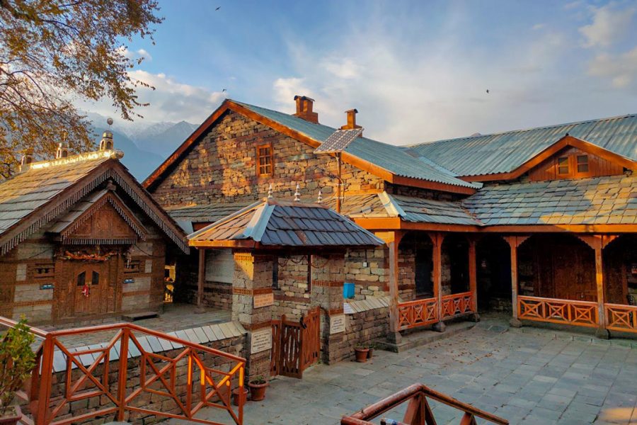 Naggar Castle in Kullu during sunset with its distinctive stone and wood architecture, surrounded by mountains under a clear sky.